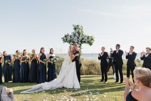 Bride and groom sharing first kiss at beach wedding ceremony with bridal party applauding.