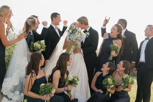 Wedding party celebrates as bride and groom kiss, bridesmaids in navy dresses hold white bouquets outdoors.