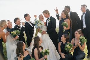 Joyful wedding party celebrating with bride and groom surrounded by bridesmaids in navy gowns and groomsmen in black tuxedos.