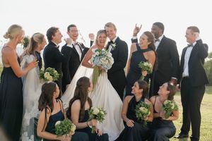 Wedding party in black and white attire posing and laughing together outdoors on a sunny day.