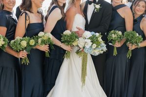 Bride and bridesmaids in navy dresses hold white and green bouquets of hydrangeas and greenery.