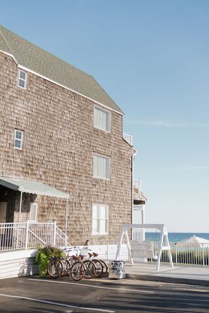 Charming cedar-shingled beachside hotel with white railings, parked bicycles, and ocean views under a clear blue sky.