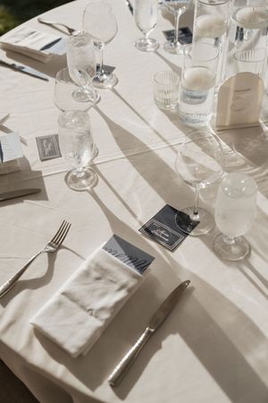 Sunlit wedding reception table with crystal glassware, silver cutlery, linen napkins, and elegant place cards.