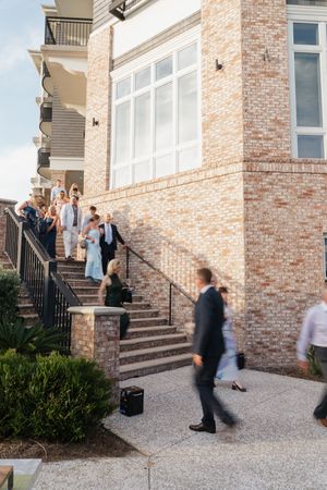 Wedding guests descend brick building stairs in golden afternoon light while others walk below.