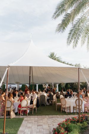 Elegant outdoor wedding reception under a white sailcloth tent with guests seated at round tables.