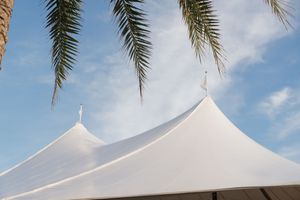 White sailcloth wedding tent framed by tropical palm tree fronds against blue sky.