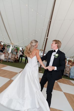 Bride and groom share their first dance under a elegant white tent with string lights at their wedding reception.