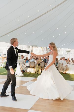 Bride and groom share their first dance on a checkered floor under a white tent at an elegant wedding reception.