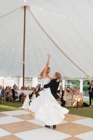 Groom lifting bride during their first dance under a white sailcloth tent at wedding reception.