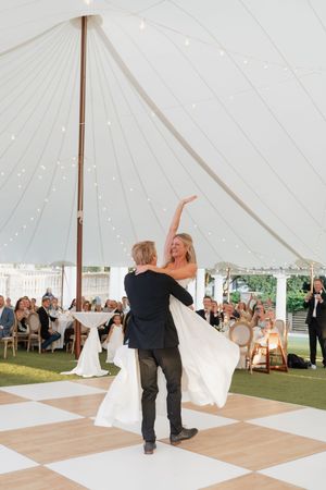 Bride and groom share first dance under elegant white tent with fairy lights at outdoor wedding reception.