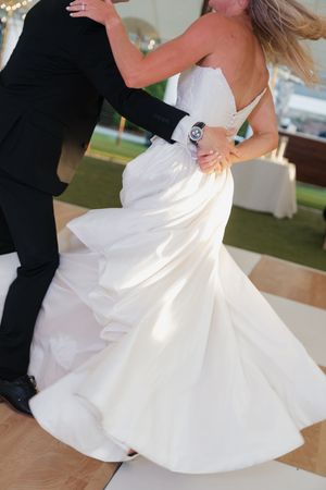 Bride in elegant mermaid wedding gown twirling with groom during first dance at outdoor wedding reception.