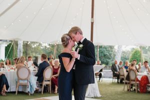 Groom shares a tender mother-son dance at an elegant tented wedding reception with seated guests in background.