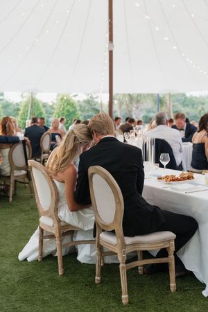 Bride and groom share intimate moment seated at sweetheart table during elegant outdoor tented wedding reception.