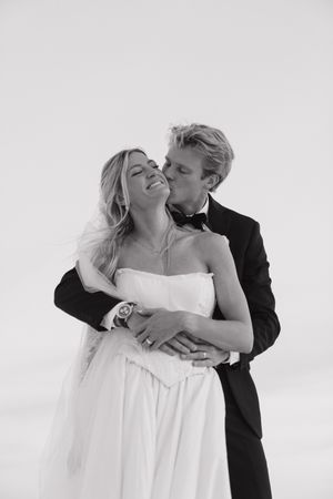 Black and white romantic photo of groom kissing bride on cheek as she smiles joyfully.