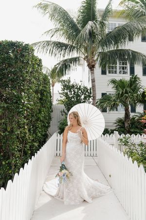 A bridal portrait with white parasol against tropical landscaping and white picket fence.