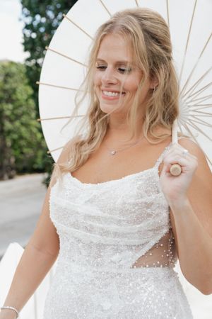 A white parasol complements the sparkly wedding dress in outdoor bridal portraits.