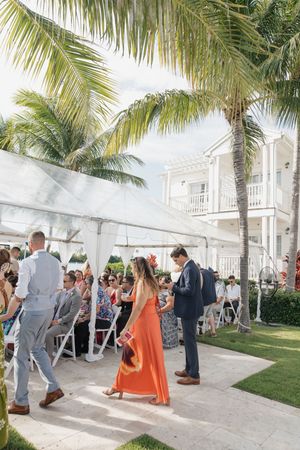Wedding guests mingle on a palm-lined patio during an outdoor reception at a tropical venue.