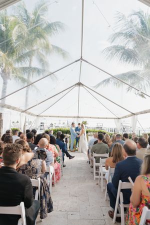 Wedding ceremony setup under a white tent with palm trees and ocean views.