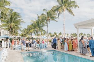 Outdoor wedding reception by a pool with palm trees and guests gathered under a sunny Florida sky.