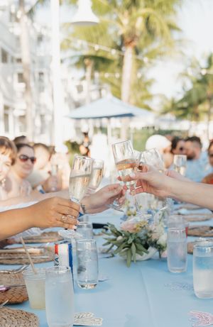Wedding guests toast with champagne glasses at an outdoor reception table decorated with floral centerpieces.