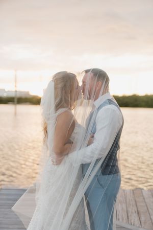 Romantic sunset beach wedding photos with flowing veil creating dreamy silhouettes.