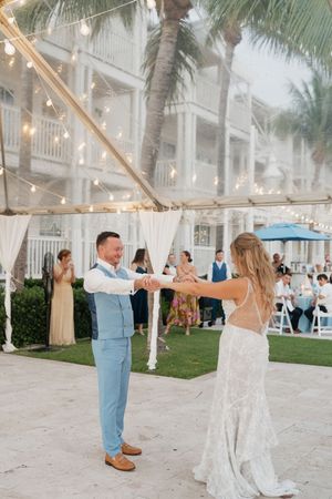 Wedding couple dancing and twirling on a patio with string lights and palm trees.