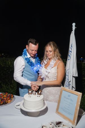 Newlyweds cut their white wedding cake together at their reception.