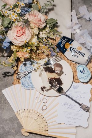Wedding details featuring paper fans, floral arrangements, and wedding rings displayed on a light surface.