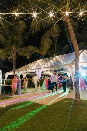 Outdoor wedding reception tents lit up at night with string lights and palm trees.