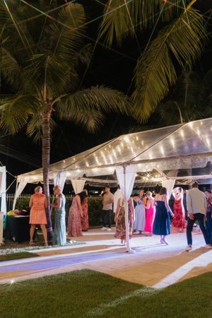 Wedding guests dancing under a lit tent with palm trees in the evening.