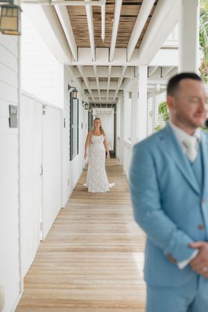 A couple shares a first look moment in a bright hallway with white walls and wooden floors.