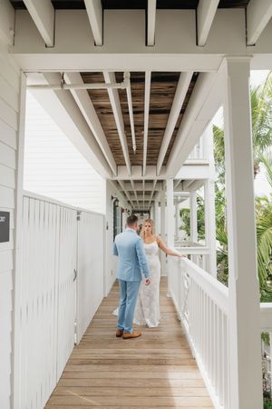 A coastal wedding scene on a white wooden walkway surrounded by palm trees.