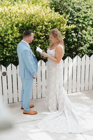 A couple exchanges vows in front of a white picket fence surrounded by lush greenery.