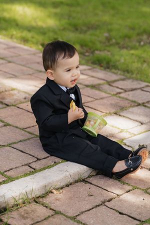 Small child in formal black attire sitting on stone pavers in an outdoor setting.