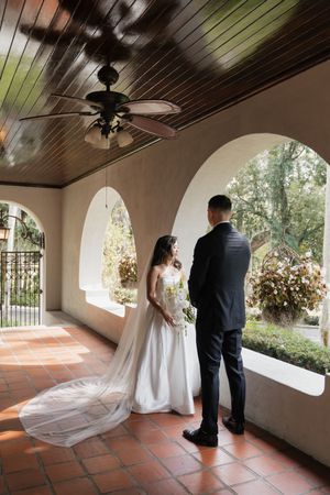 A bride and groom share a private moment under an arched porch with terracotta tiles and wooden ceiling.