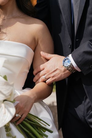 Elegant couple holding hands and a white floral bouquet during wedding ceremony.