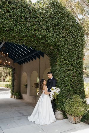 Wedding couple sharing a moment under an ivy-covered pergola with string lights.