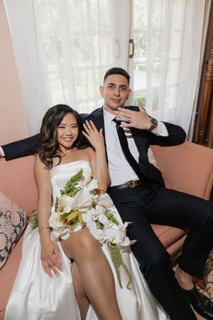 Playful wedding portraits captured indoors showing couple in formal attire with white bouquet.