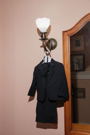 A black formal suit jacket hangs from an ornate wall sconce with white glass shade.