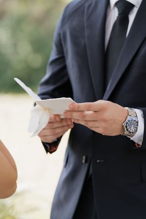 Close-up of hands holding wedding vows during an outdoor ceremony.