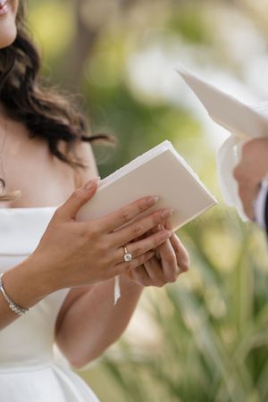 A series of hands holding and reading from white books or papers in a wedding setting.