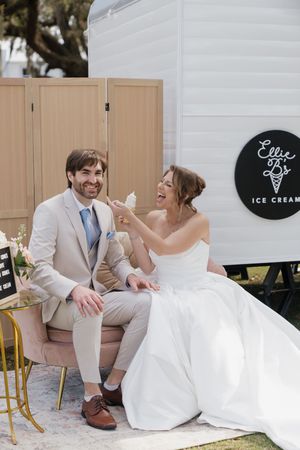 A wedding couple shares ice cream at an outdoor reception with rustic decor and wooden doors.