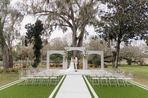 White wedding ceremony setup with a gazebo and rows of chairs on a manicured lawn surrounded by Spanish moss-draped trees.
