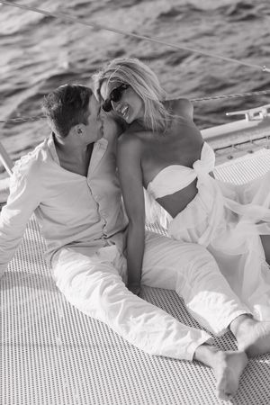 Black and white photo of a romantic couple relaxing together on a luxury sailboat deck over ocean waters.