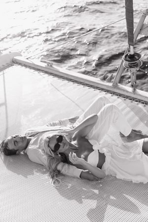 Black and white aerial view of a loving couple lying together on a catamaran net over sparkling water.