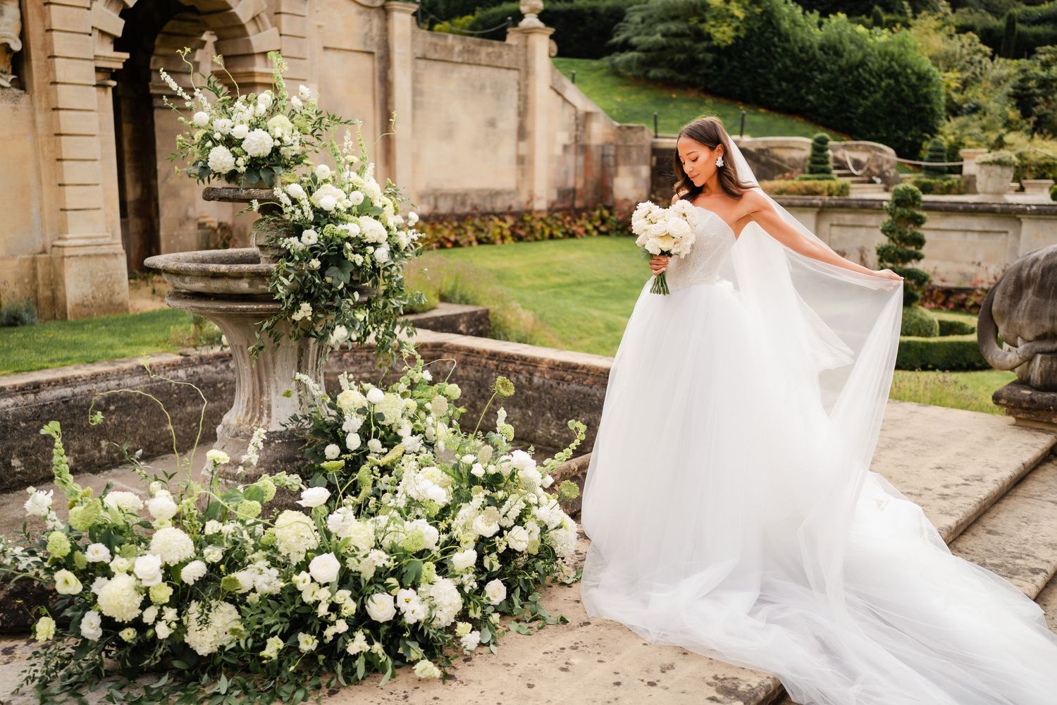 Wedding photography series in garden setting with white floral arrangements and stone architecture.