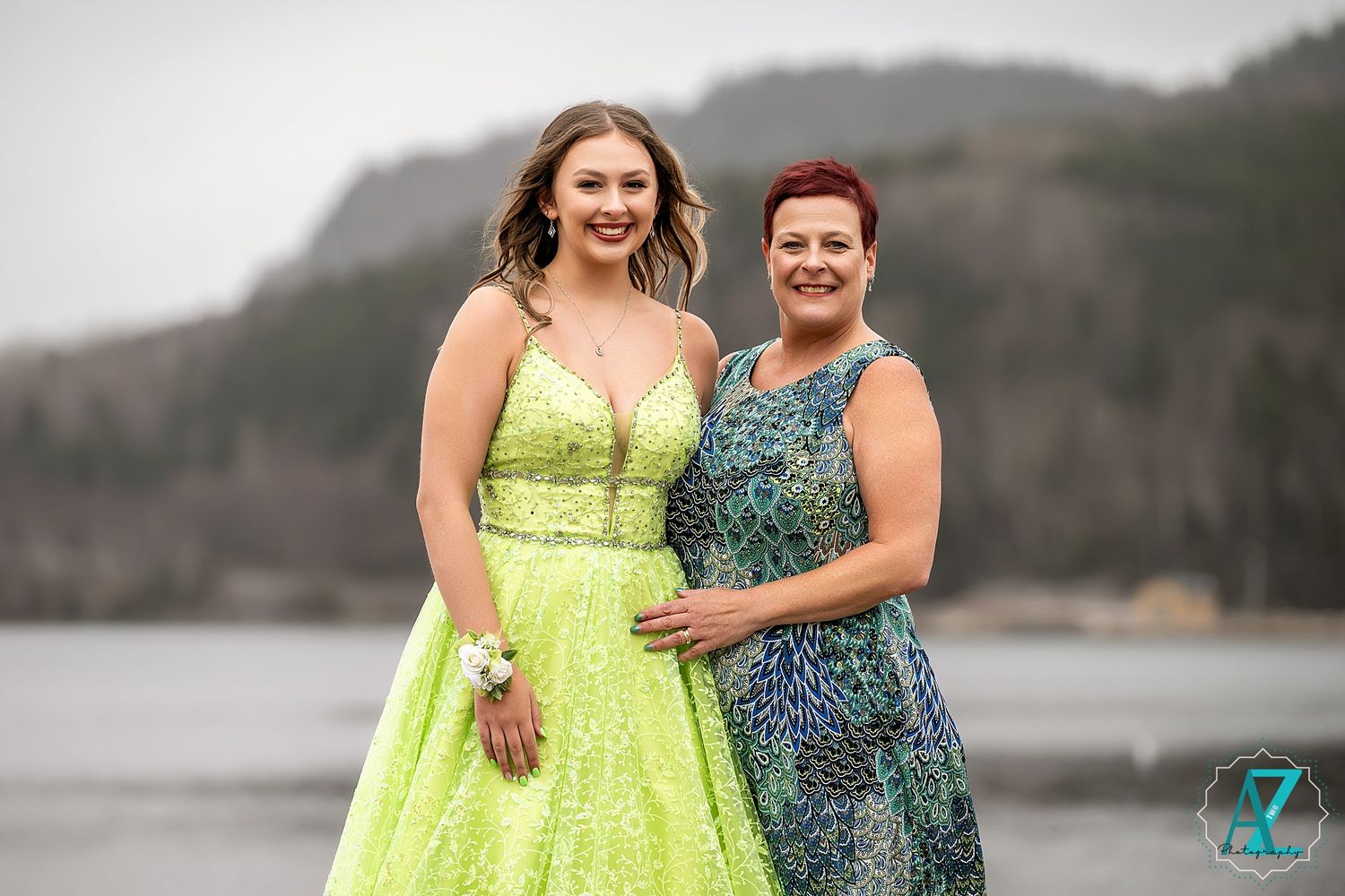 Two people pose together against a waterfront backdrop, one wearing a lime sequined gown and another in blue.
