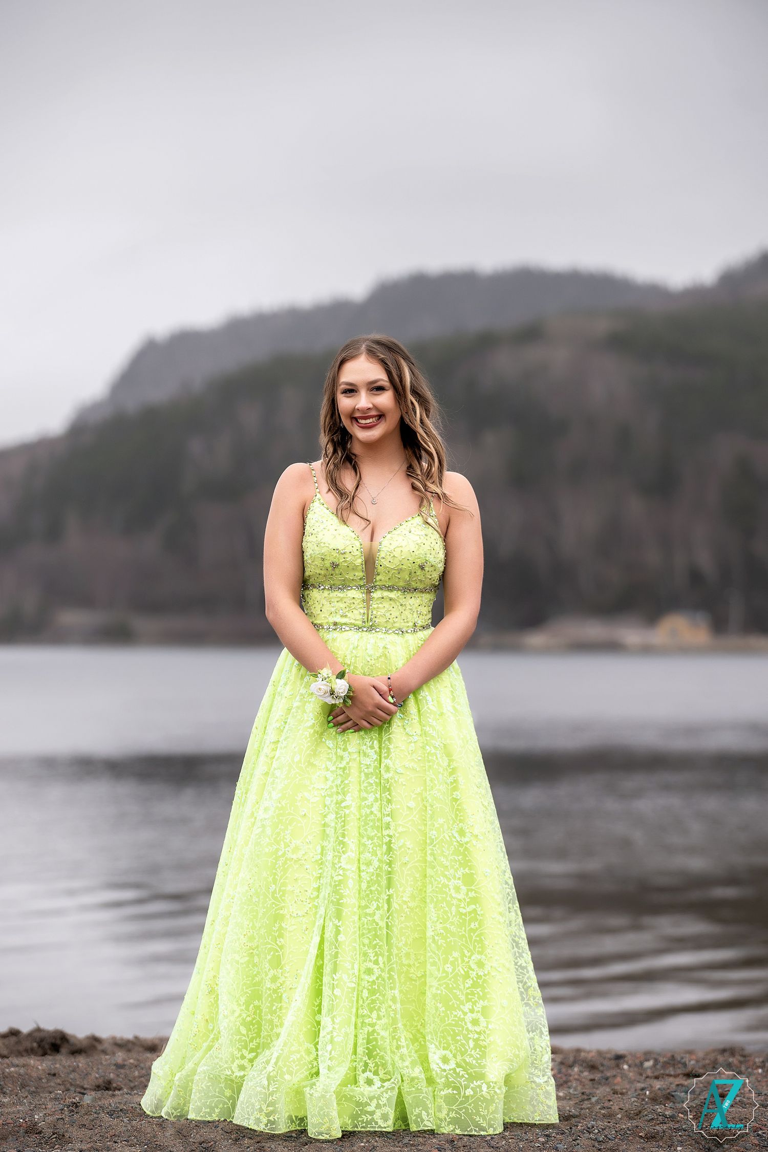 A person in a stunning lime green sequined ball gown poses by a waterfront with mountains in the background.