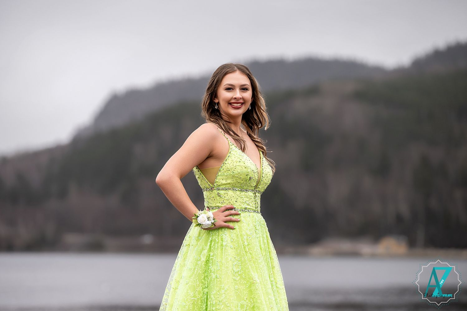 Someone poses confidently in a sparkly lime green formal gown against a scenic waterfront backdrop.