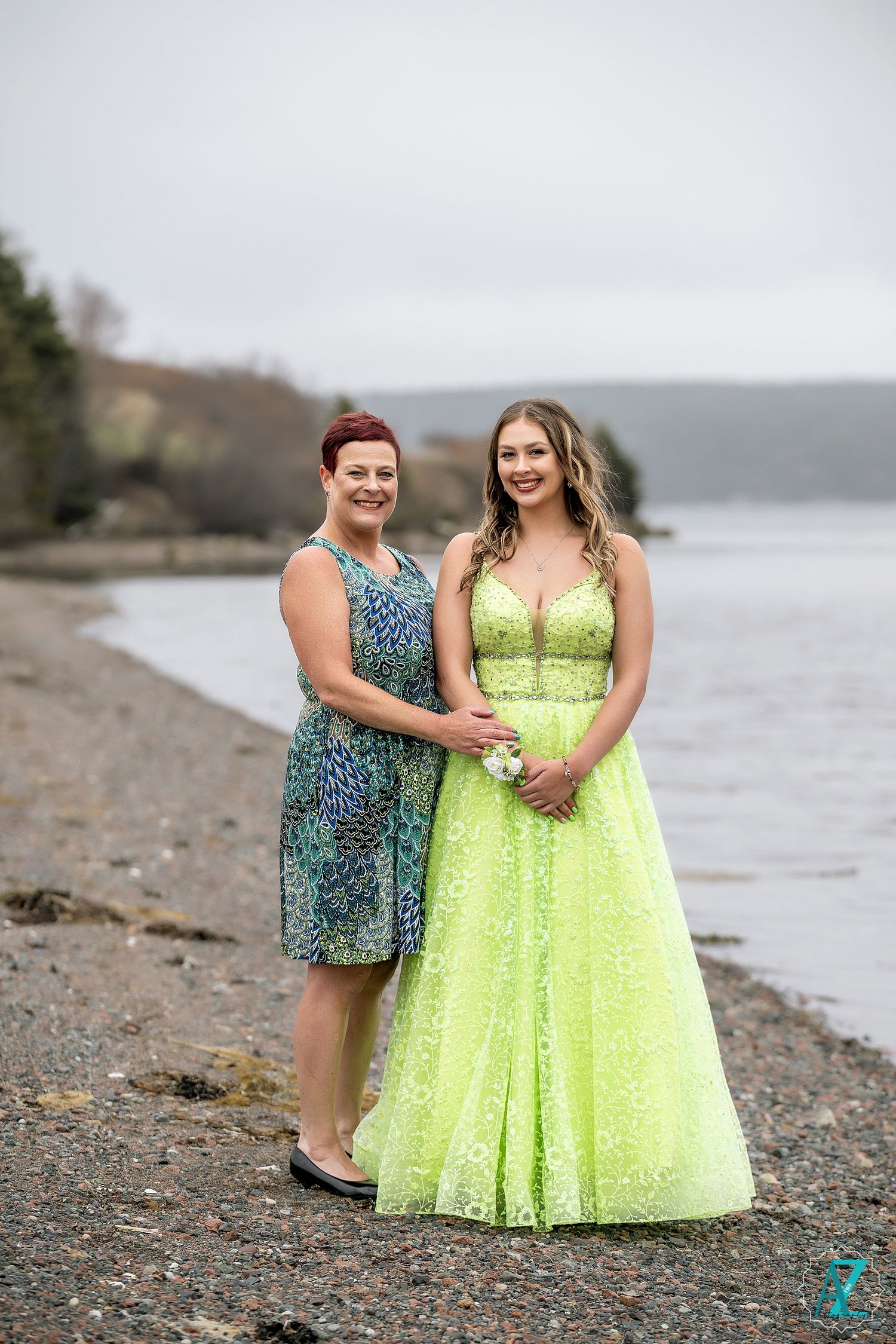Two people pose together on a rocky beach, wearing complementary formal dresses in lime and blue.